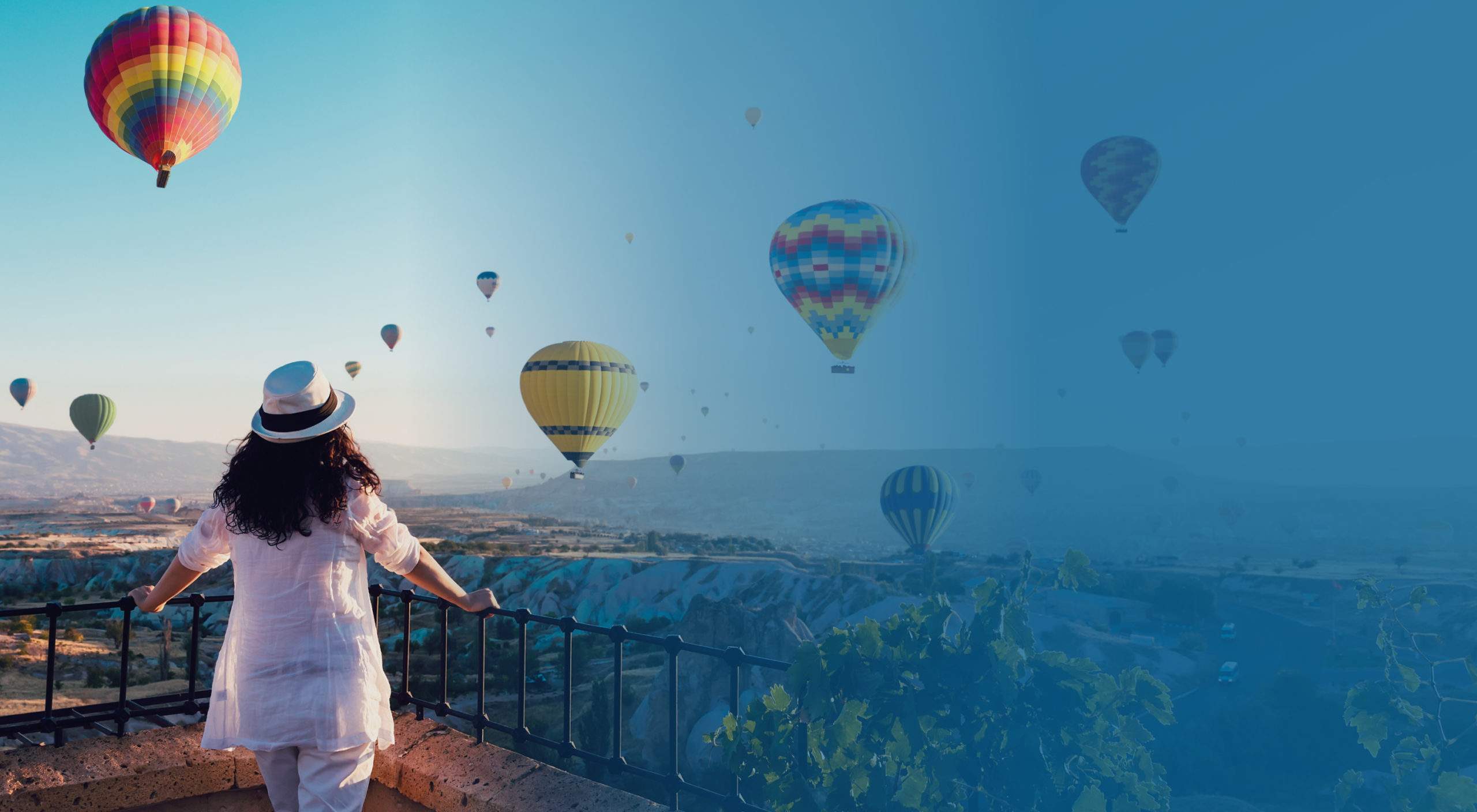 A woman watching several hot air balloons float across a wide canyon
