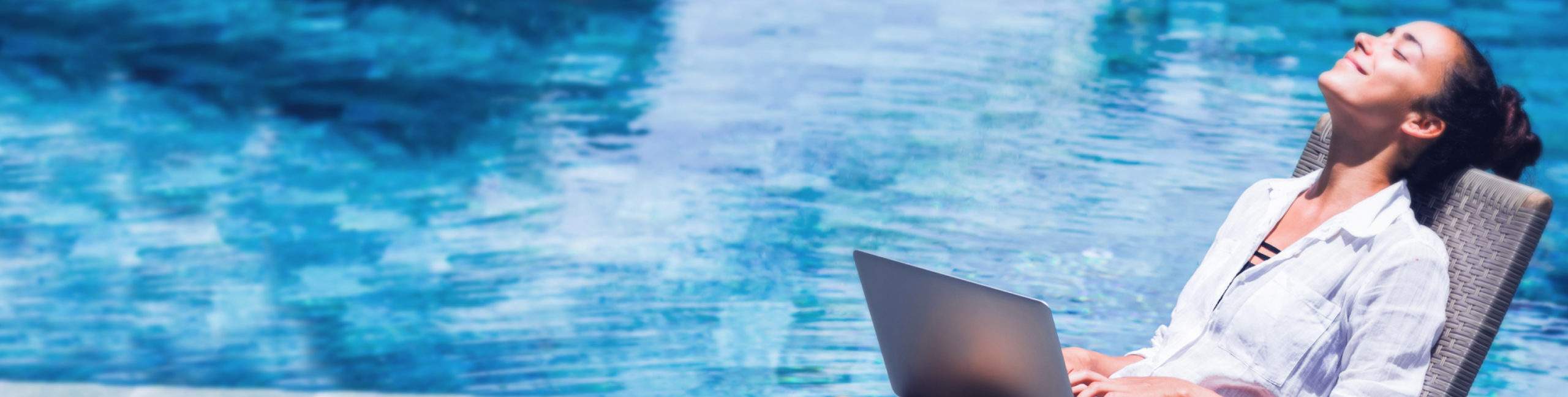 A woman lounging by a pool with a laptop