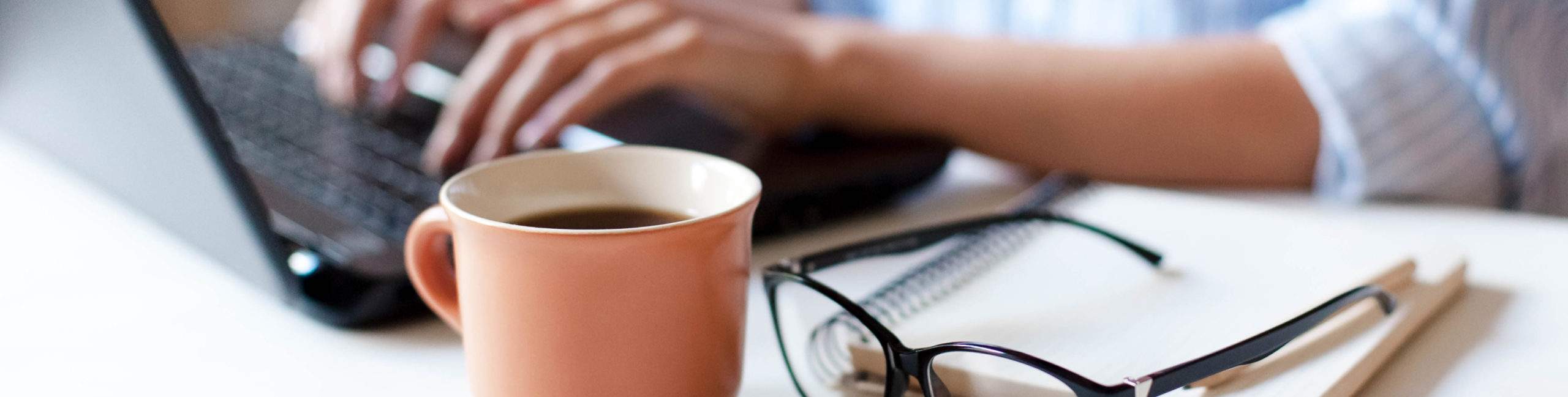 A mug of coffee alongside someone working at their laptop