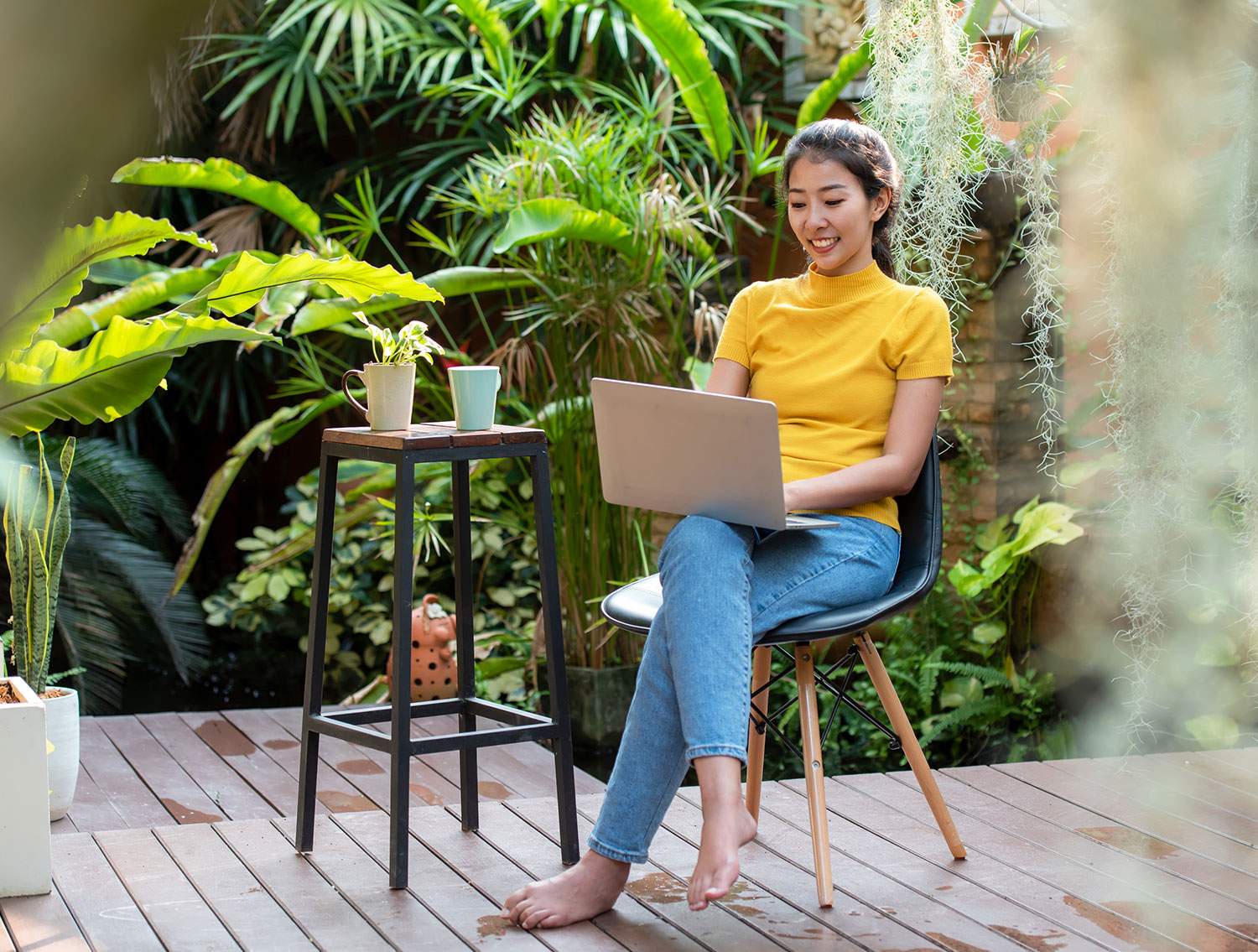 Woman smiling and working laptop in a garden - learn how to travel and work remotely