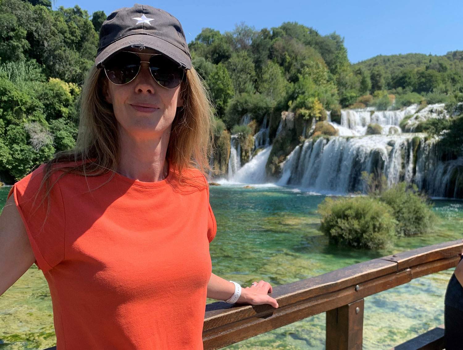 Woman with hat posing with a waterfall in the background