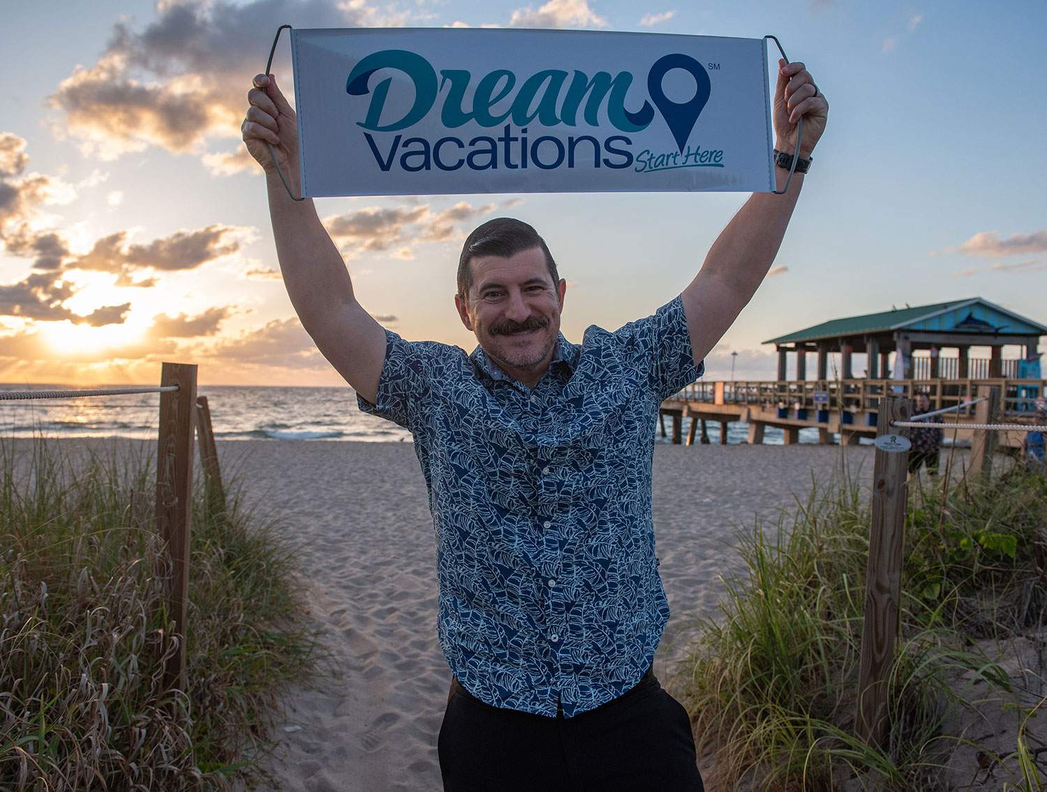 man holding Dream Vacations sign over his head on beach