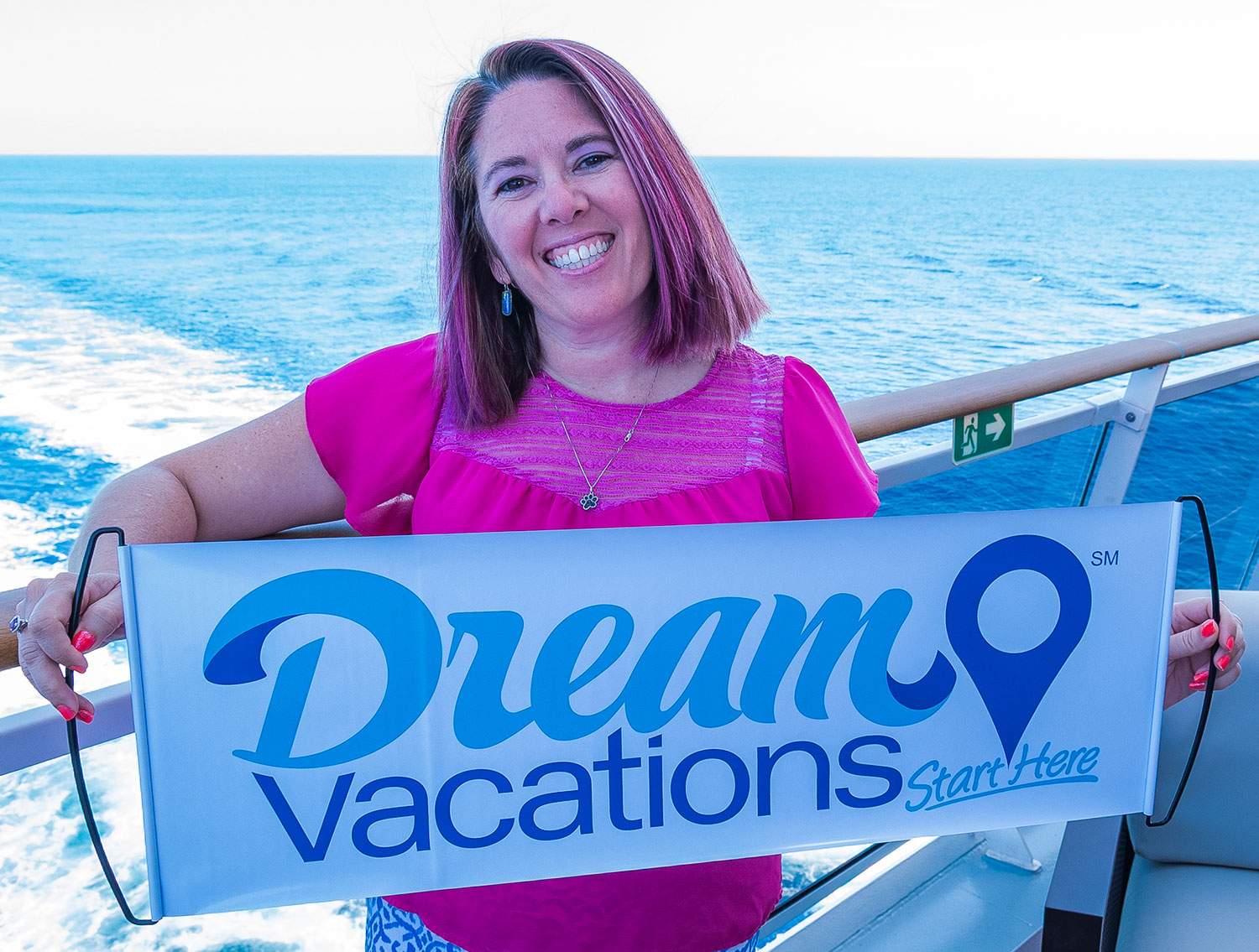 woman with pink hair holding Dream Vacations sign on ship