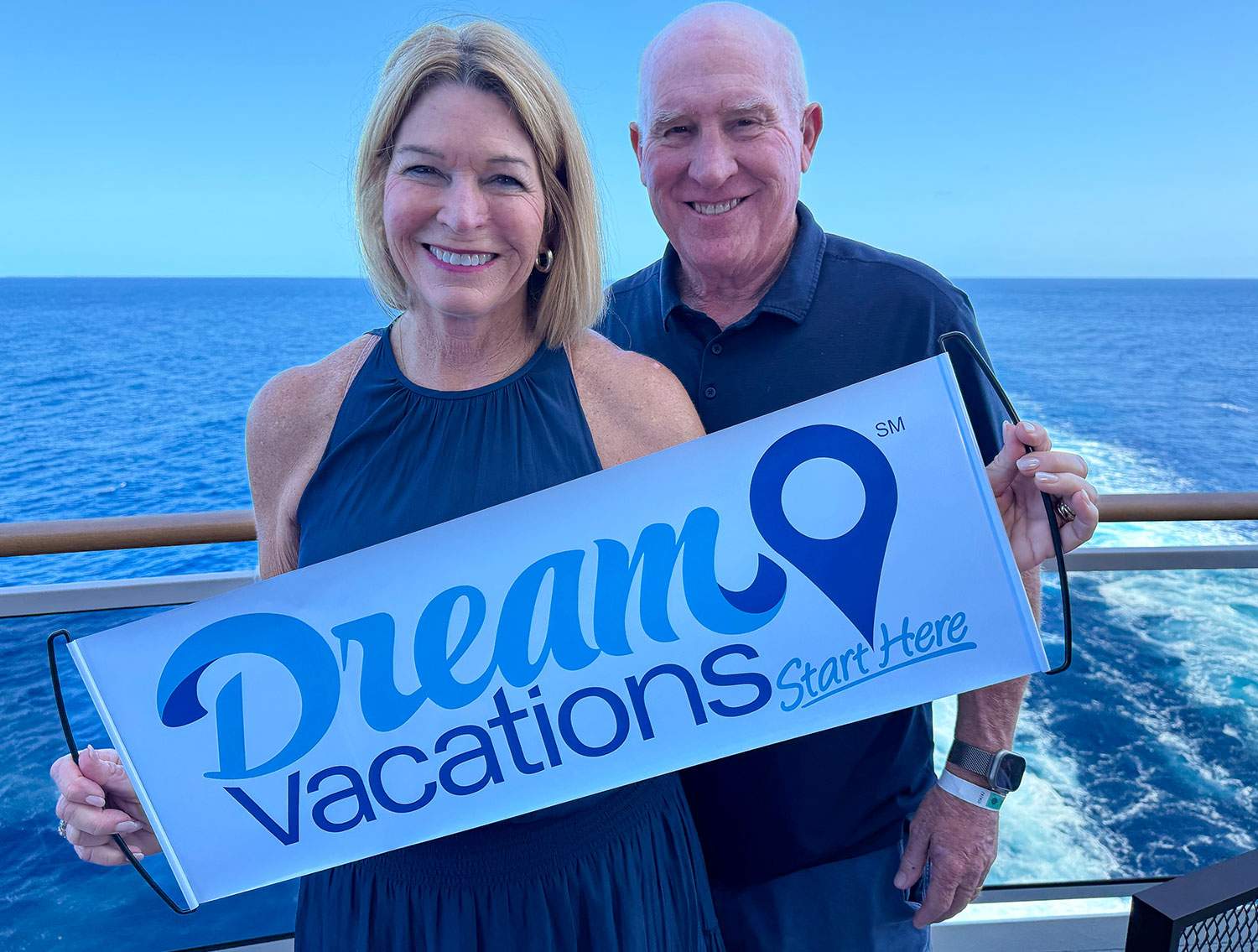 A man and woman smiling while holding a sign that reads Dream Vacations.