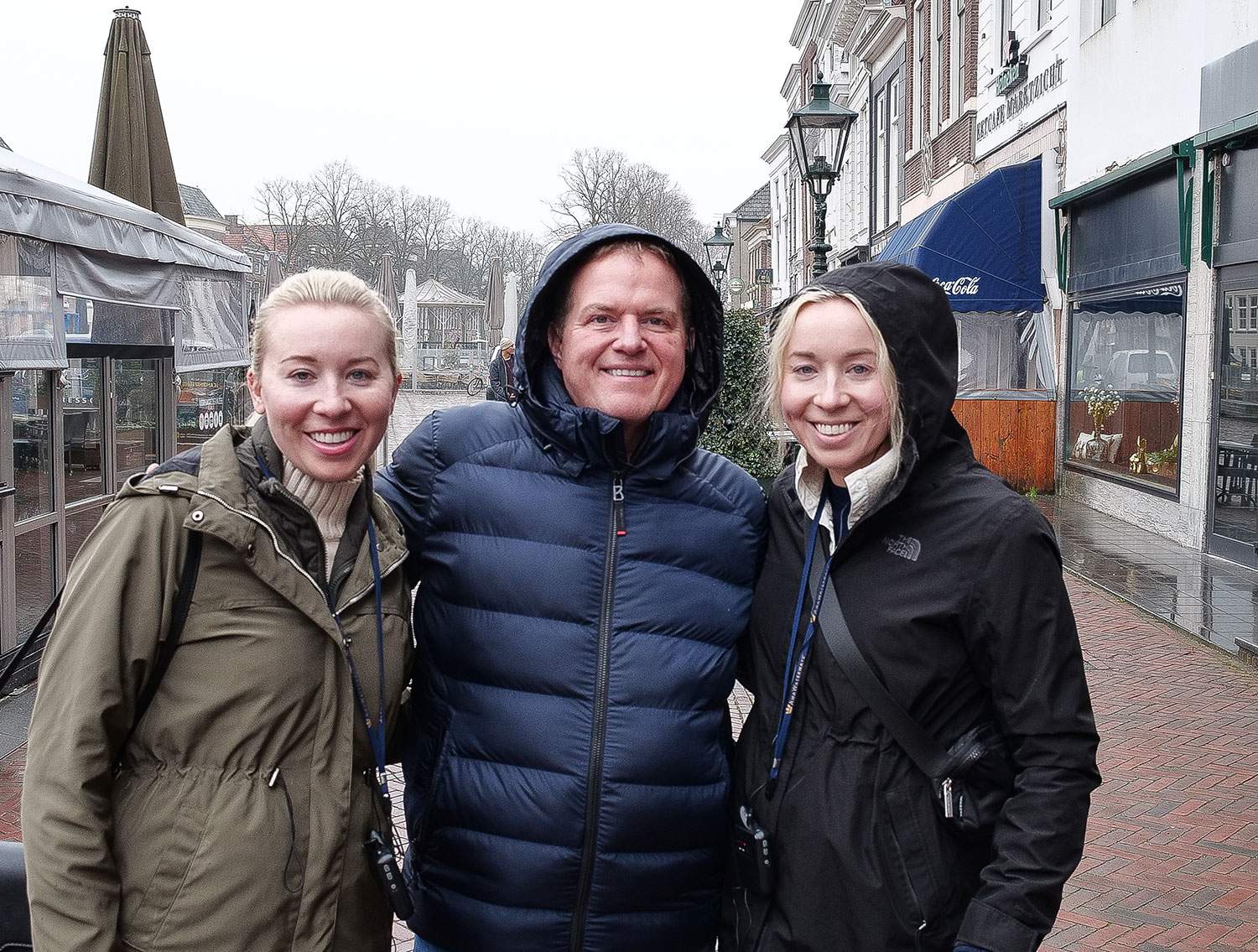 A man and two women stand together on a brick street, smiling