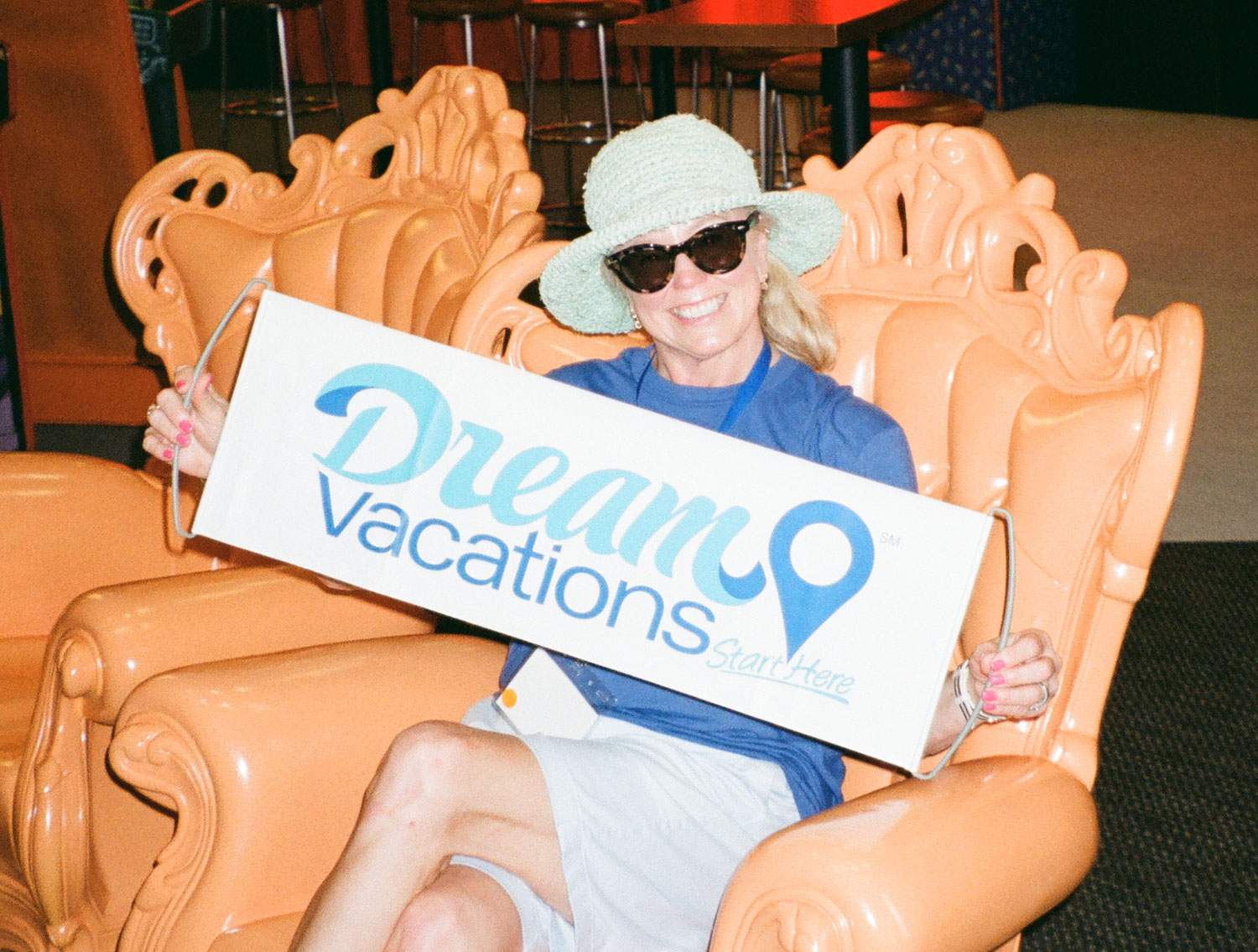 A woman sitting in a chair, holding a Dream Vacations sign.