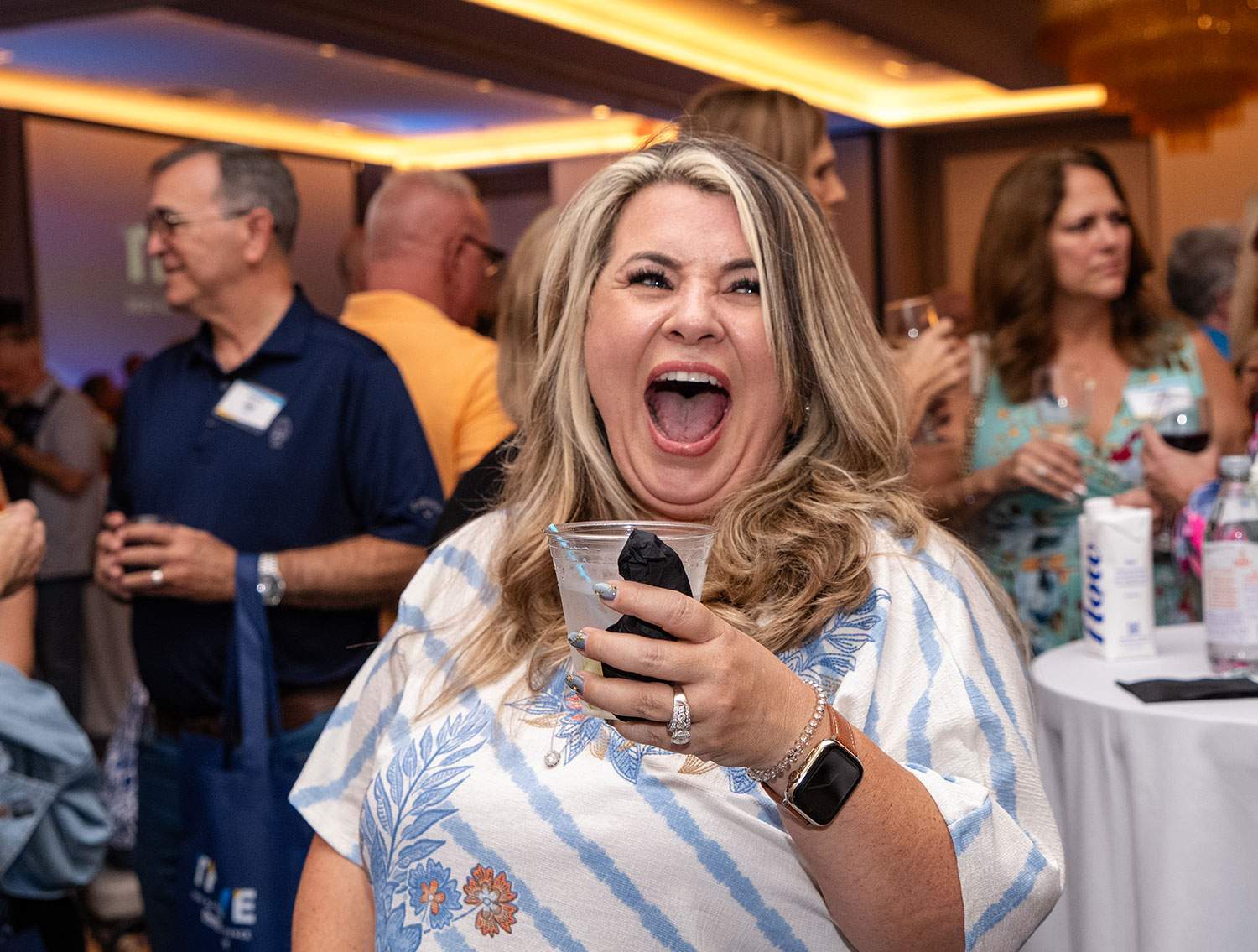 A woman laughs joyfully while holding a drink in her hand.